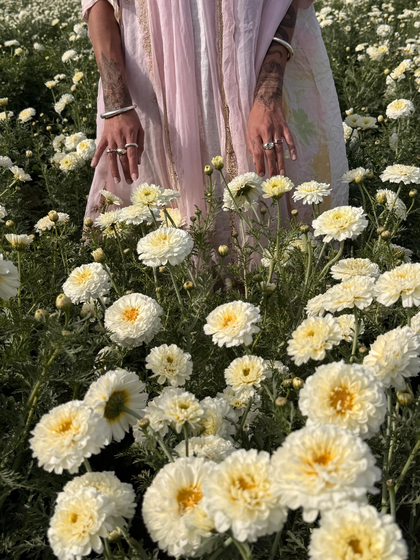 Akasha's hands wearing handmade jewelry among white flowers